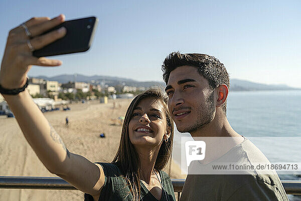 Smiling young woman taking selfie with boyfriend through smart phone