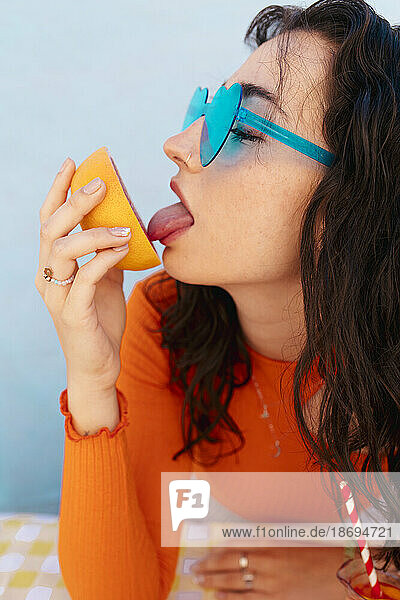 Woman wearing heart shape sunglasses licking grapefruit