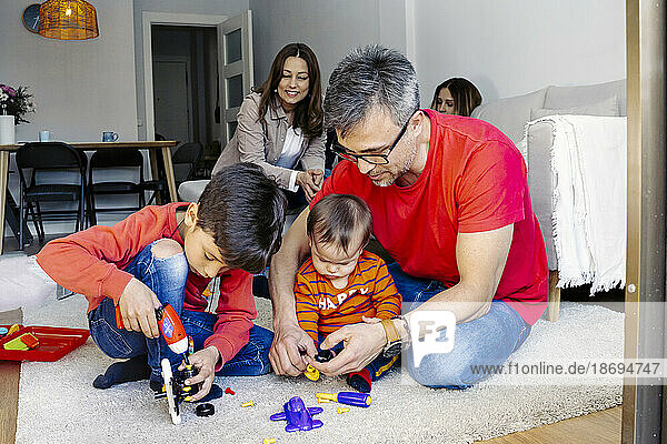 Vater sitzt neben Söhnen und spielt mit Spielzeug im Wohnzimmer zu Hause
