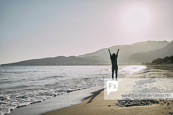 Fröhliche Frau  die mit erhobenen Armen in Ufernähe am Strand spaziert
