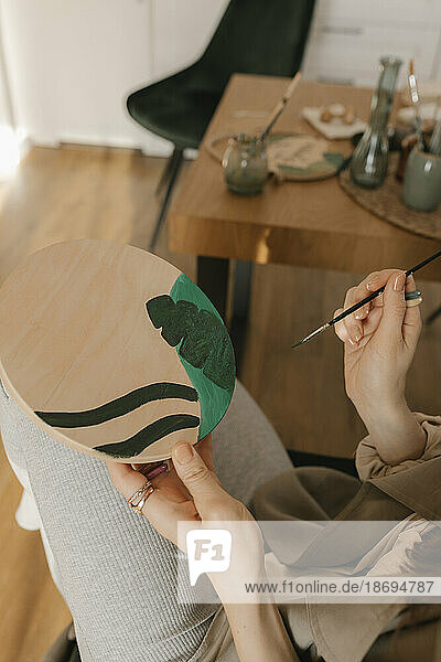 Frau malt auf Holzbrett und sitzt am Tisch