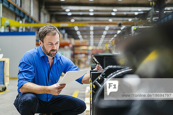 Mature businessman with document examining machine at factory