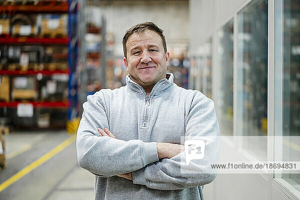 Smiling mature employee with arms crossed at factory