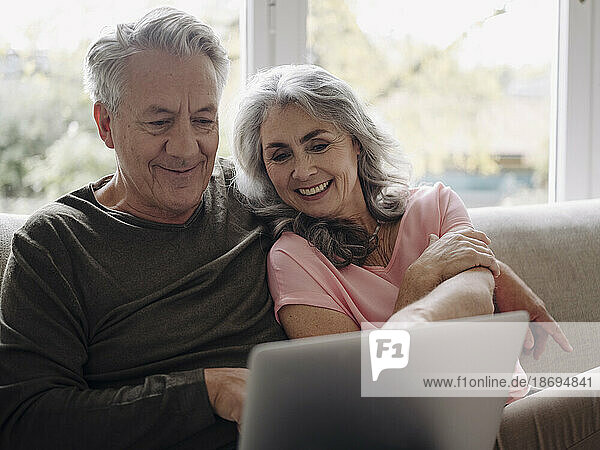 Glückliches älteres Paar mit Laptop  das es sich zu Hause auf der Couch gemütlich macht