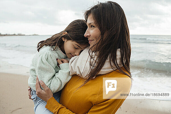 Smiling woman carrying daughter at beach
