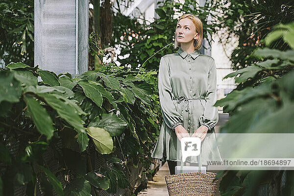 Woman with bag standing in greenhouse