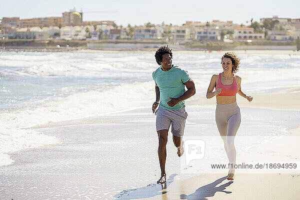 Smiling couple jogging together at beach