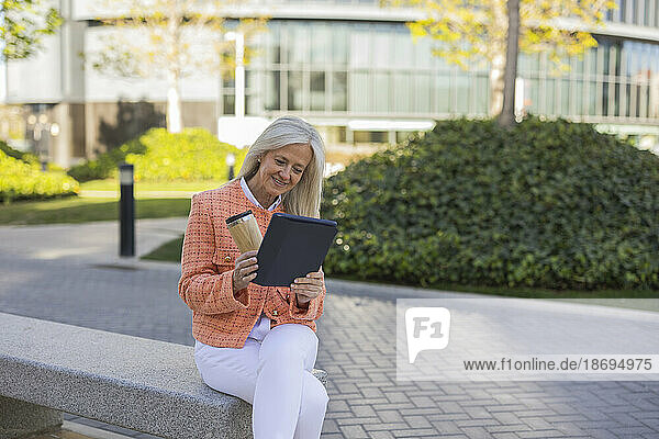 Lächelnde Geschäftsfrau  die auf einer Bank sitzt und einen Videoanruf über einen Tablet-PC tätigt