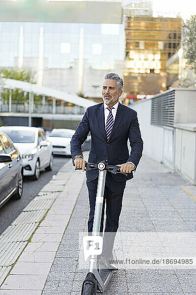 Businessman commuting through electric scooter on sidewalk