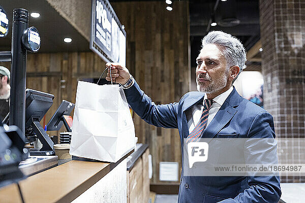 Businessman holding shopping bag standing at cafe counter