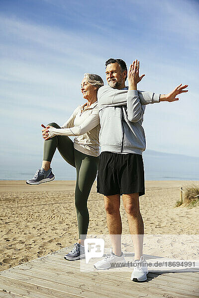 Woman stretching with man standing at beach