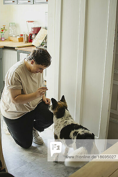 Non-binary person feeding dog in kitchen at home