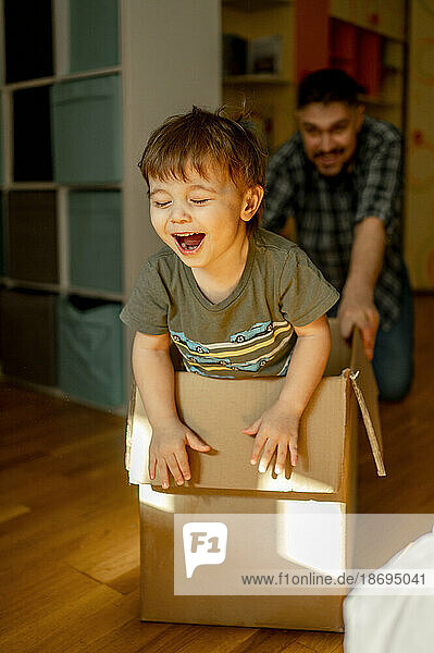 Playful father pushing son in cardboard box at home