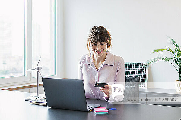 Smiling businesswoman with credit card sitting at desk