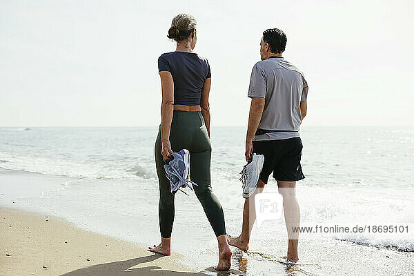 Couple holding sports shoes walking near shore at beach