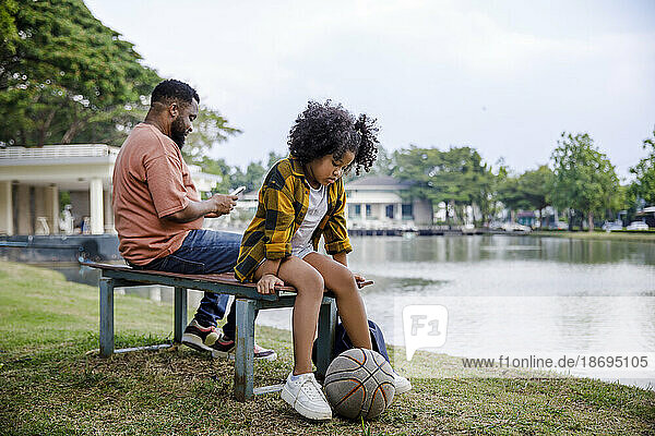Girl with basketball sitting on bench by father at park