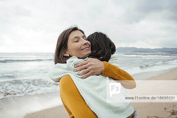 Smiling woman hugging daughter at beach