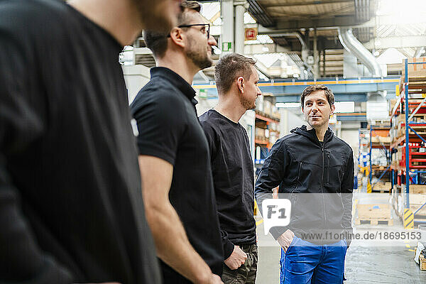 Employees with hands in pockets discussing in meeting at factory
