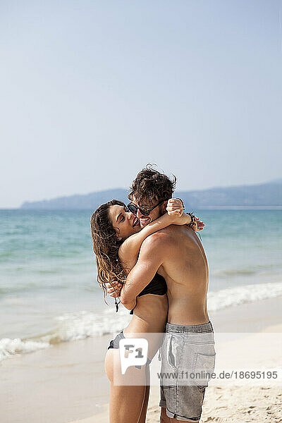 Mann umarmt Frau im Bikini am Strand