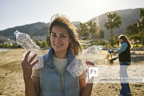 Smiling woman holding crumpled plastic bottles at beach