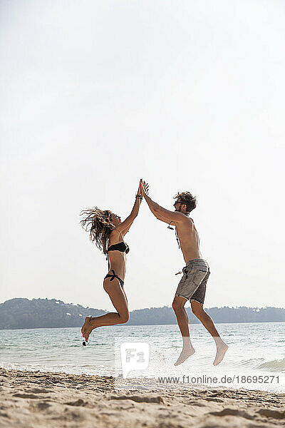 Happy couple giving high-five jumping at beach