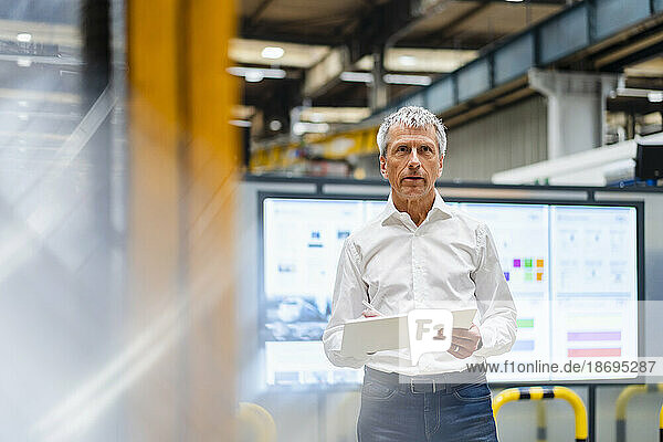 Businessman standing with tablet PC and examining in factory