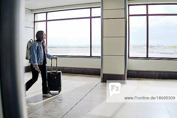 Young woman with suitcase walking at airport lobby