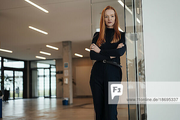 Businesswoman with arms crossed leaning on wall at office
