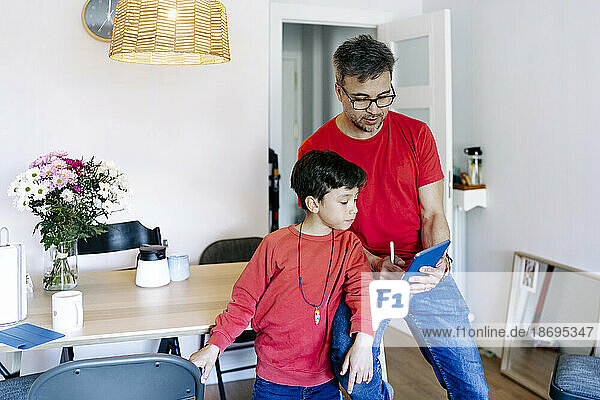 Son standing by father using tablet PC at home