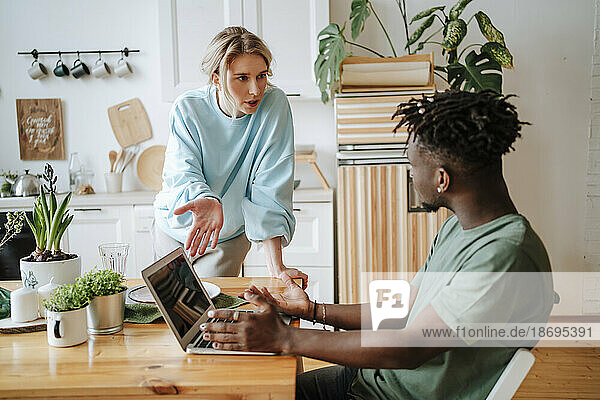 Frau diskutiert mit Mann  der zu Hause Laptop benutzt