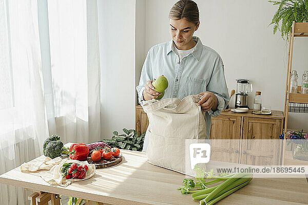 Woman removing fruits from reusable bag on table at home