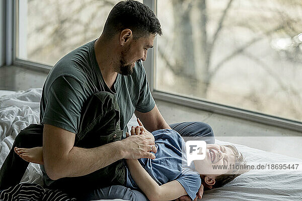 Father tickling son lying on bed at home