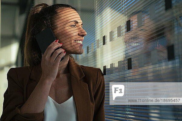 Businesswoman talking on smart phone looking out of window at office