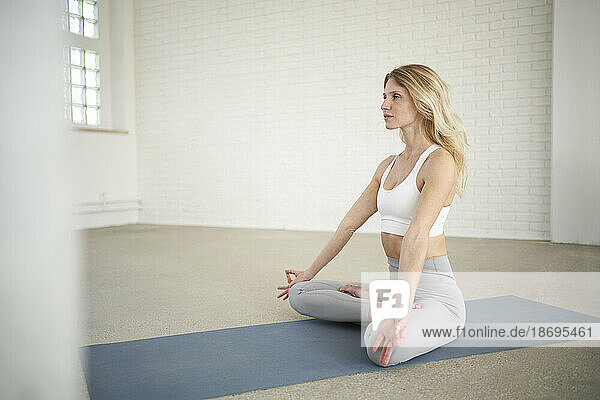 Young woman sitting cross-legged and practicing yoga in studio
