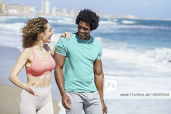 Fröhliches Paar in Sportkleidung spaziert am Strand