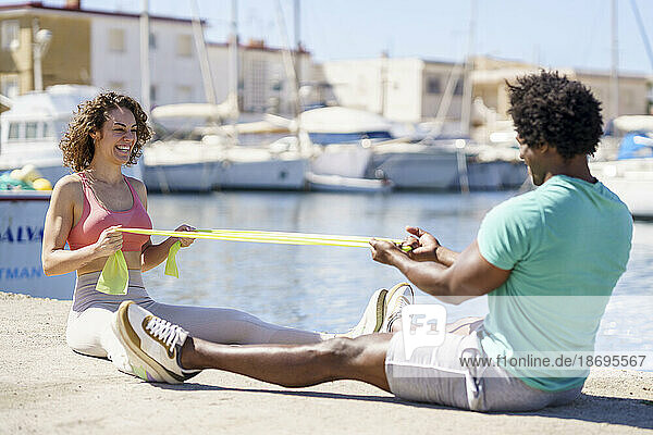 Happy couple exercising with resistance band on pier at harbour