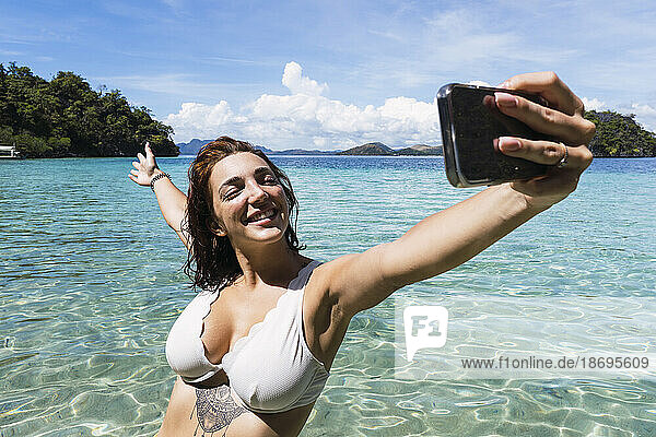 Carefree woman taking selfie through smart phone in sea at vacation