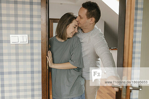 Mann küsst Frau  die zu Hause an der Tür steht