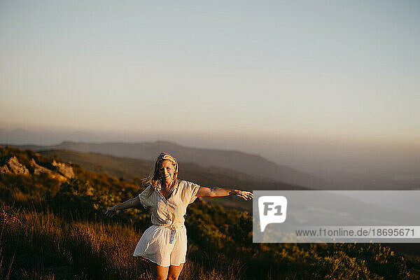 Smiling woman standing with arms outstretched on mountain