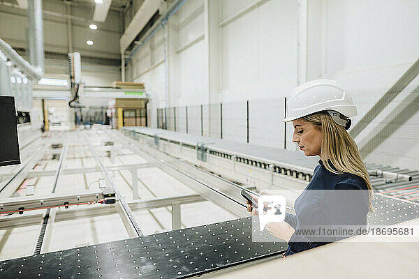 Businesswoman using smart phone standing in production hall at factory
