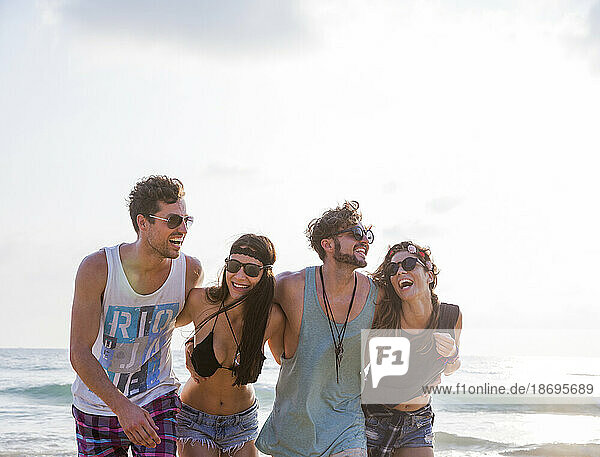 Happy friends laughing with arms around at beach