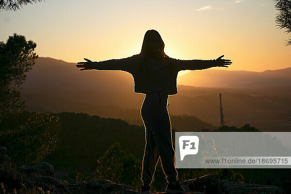 Silhouette of woman with arms outstretched at sunset