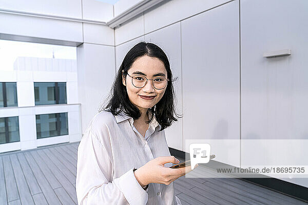 Portrait of young businesswoman with mobile phone on terrace of office building