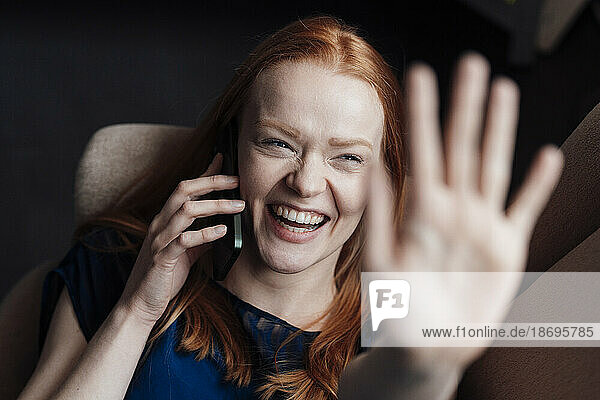 Glückliche Frau zeigt Handfläche und spricht mit Smartphone