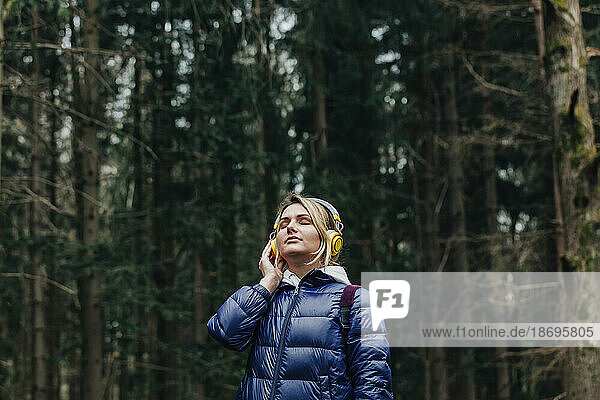 Young woman enjoying music through headphones in forest