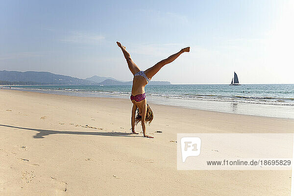 Young woman in bikini practicing handstand at beach