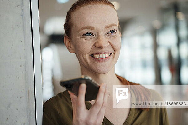 Happy businesswoman talking on speaker phone at office