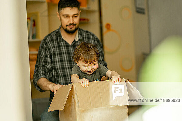 Father looking at son playing in cardboard box at home