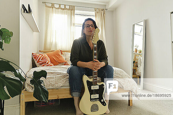 Frau sitzt mit Gitarre zu Hause im Bett
