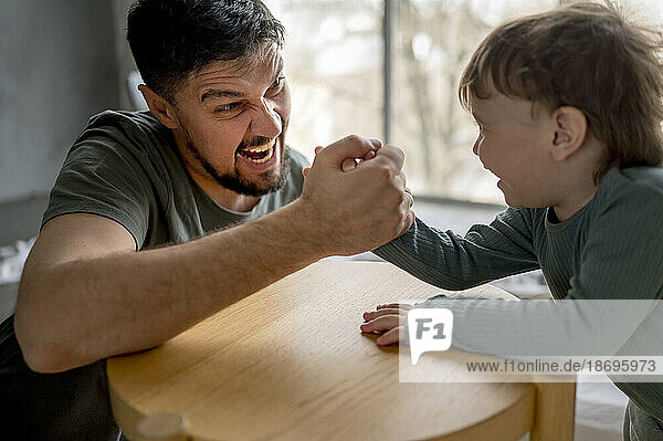 Excited father arm wrestling with son at home